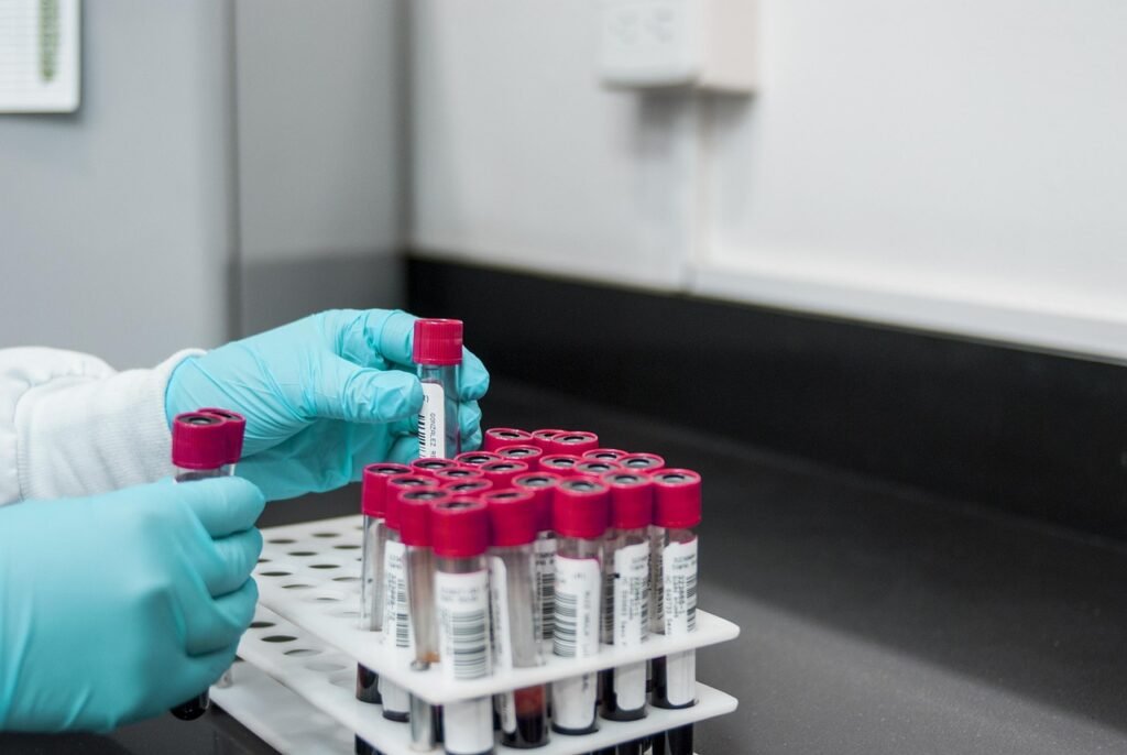 Technician with blue gloves handles red-capped vials on a black lab counter.